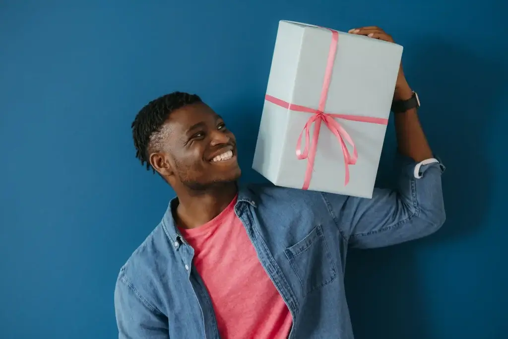 Bonito jovem africano em traje casual carregando caixa de presente no ombro e sorrindo